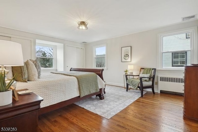 bedroom with radiator, multiple windows, and wood finished floors