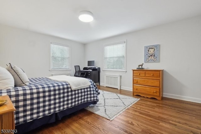 bedroom featuring radiator heating unit, multiple windows, baseboards, and wood finished floors