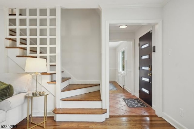 foyer with ornamental molding, wood finished floors, baseboards, and stairs