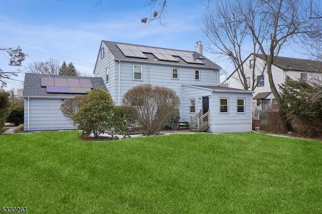 rear view of house featuring entry steps, a yard, a chimney, and roof mounted solar panels