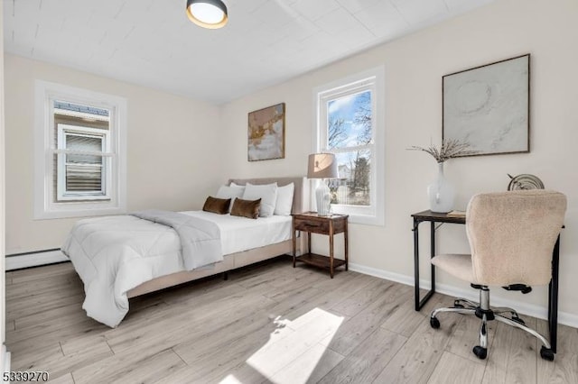 bedroom featuring a baseboard heating unit, light wood-style flooring, and baseboards