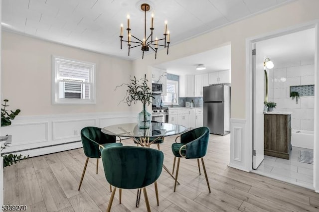 dining area with a baseboard heating unit, a wainscoted wall, a decorative wall, and light wood-style flooring