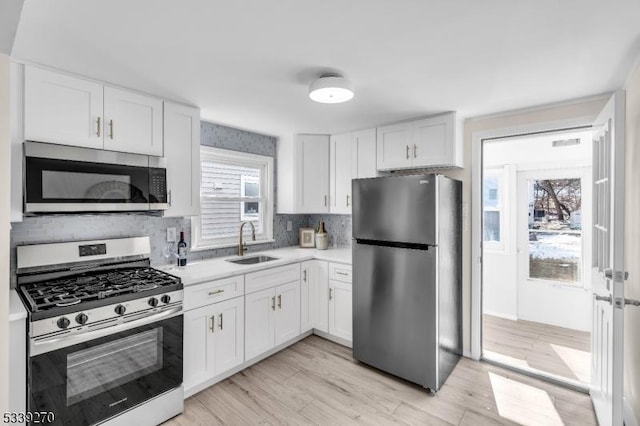 kitchen with tasteful backsplash, white cabinets, stainless steel appliances, light countertops, and a sink