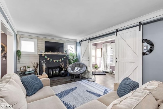 living room with a barn door, crown molding, wood finished floors, and a glass covered fireplace