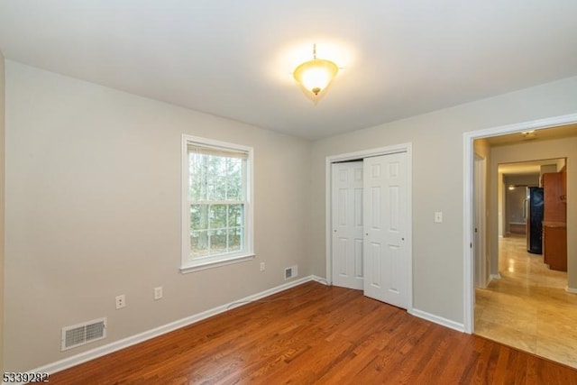 unfurnished bedroom with a closet, visible vents, baseboards, and wood finished floors