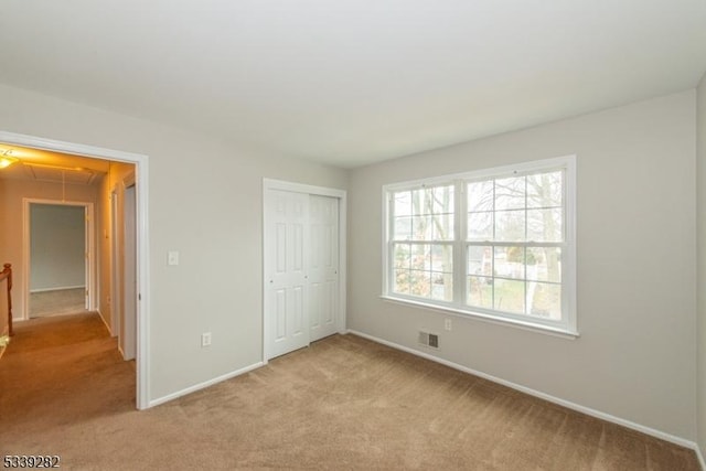 unfurnished bedroom with attic access, baseboards, visible vents, light colored carpet, and a closet