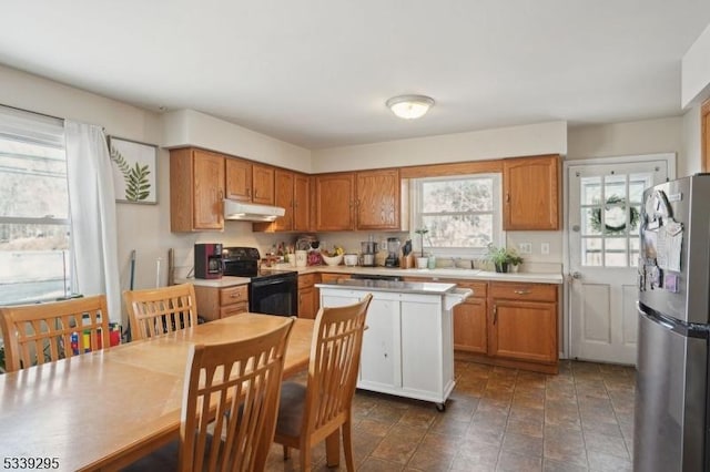 kitchen featuring black range with electric cooktop, under cabinet range hood, light countertops, freestanding refrigerator, and brown cabinets