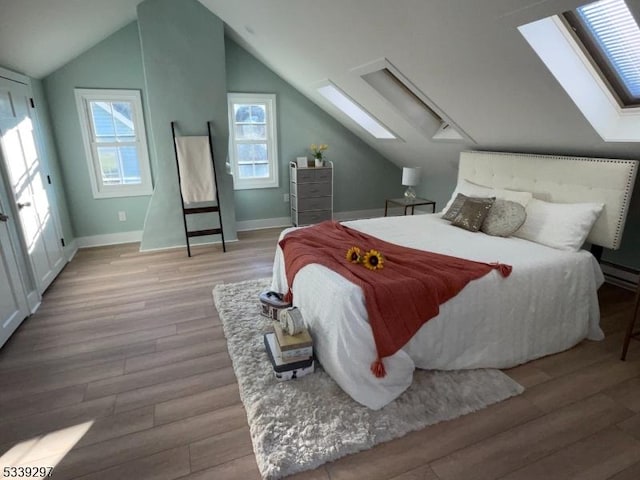 bedroom featuring a baseboard heating unit, baseboards, wood finished floors, and vaulted ceiling with skylight