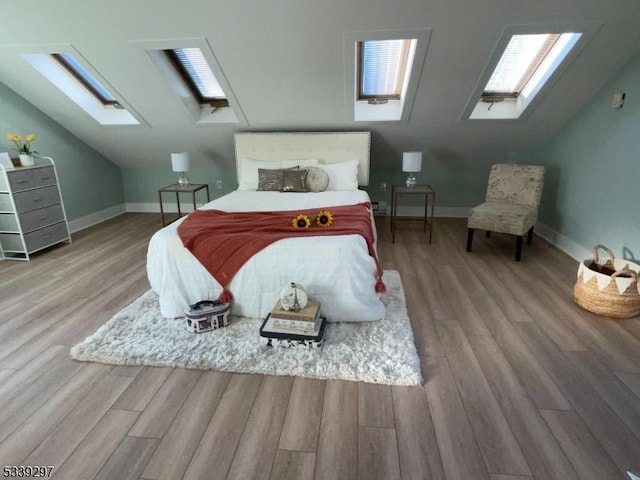 bedroom featuring lofted ceiling with skylight, wood finished floors, and baseboards