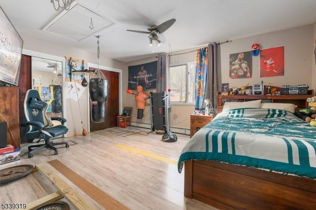 bedroom with attic access, a baseboard heating unit, and wood finished floors