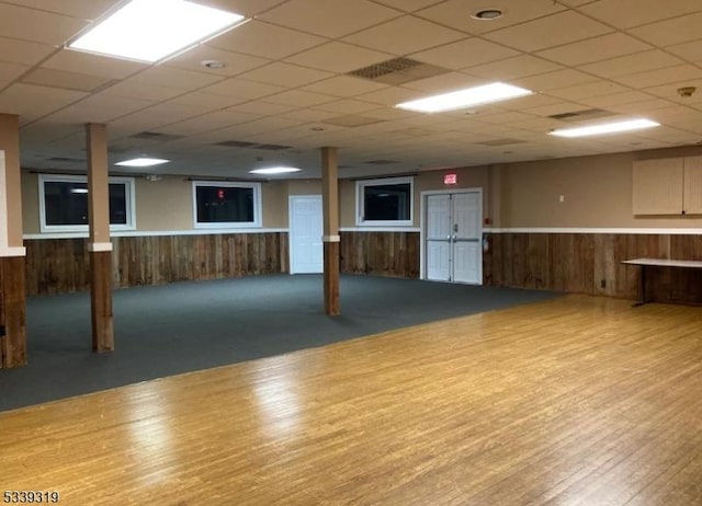 finished basement with a wainscoted wall, wood walls, a drop ceiling, and wood finished floors