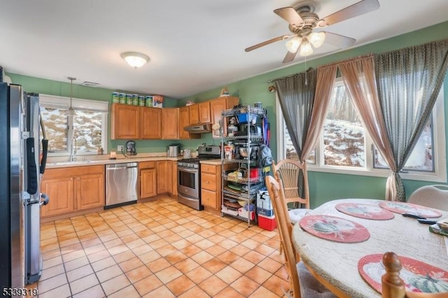 kitchen featuring appliances with stainless steel finishes, decorative light fixtures, light countertops, under cabinet range hood, and a sink