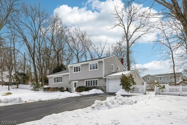 colonial-style house featuring a garage, a chimney, fence, and aphalt driveway