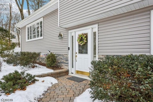 snow covered property entrance featuring stone siding