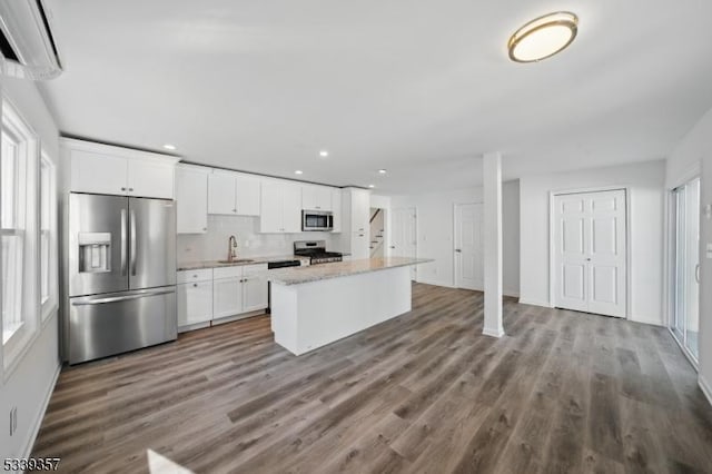 kitchen with appliances with stainless steel finishes, white cabinets, dark wood-type flooring, and a center island