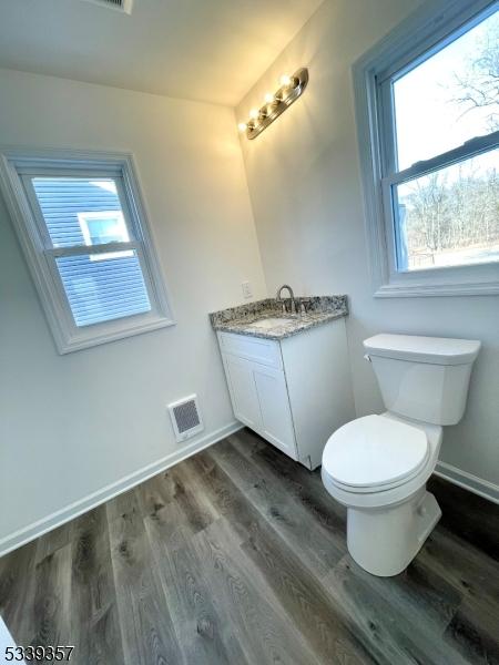 bathroom with toilet, wood finished floors, visible vents, vanity, and baseboards