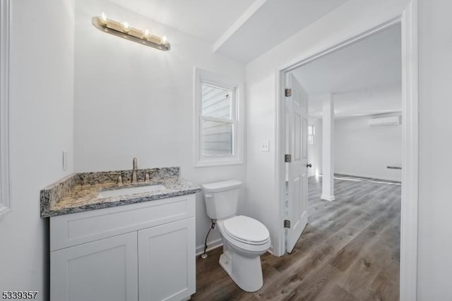 half bathroom featuring toilet, an AC wall unit, vanity, wood finished floors, and baseboards