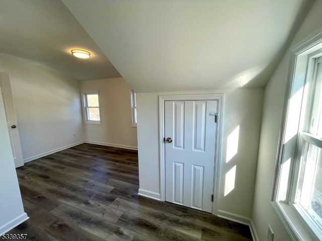 empty room featuring vaulted ceiling, baseboards, and dark wood finished floors