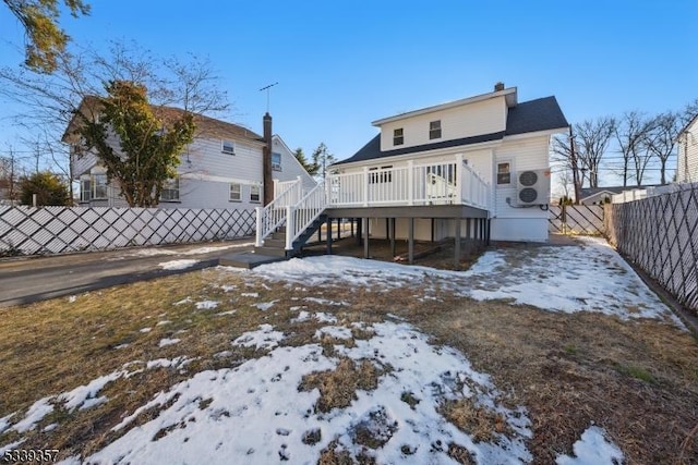 snow covered rear of property featuring a deck, a fenced backyard, and stairs