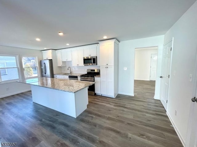 kitchen featuring white cabinets, a kitchen island, dark wood-style flooring, light stone countertops, and stainless steel appliances