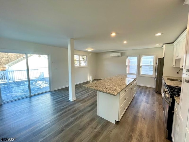 kitchen with white cabinets, a kitchen island, light stone counters, a wall mounted air conditioner, and stainless steel appliances