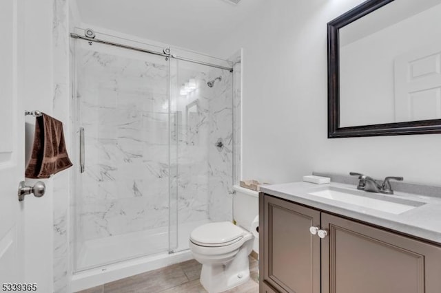 bathroom with toilet, a marble finish shower, wood finished floors, and vanity