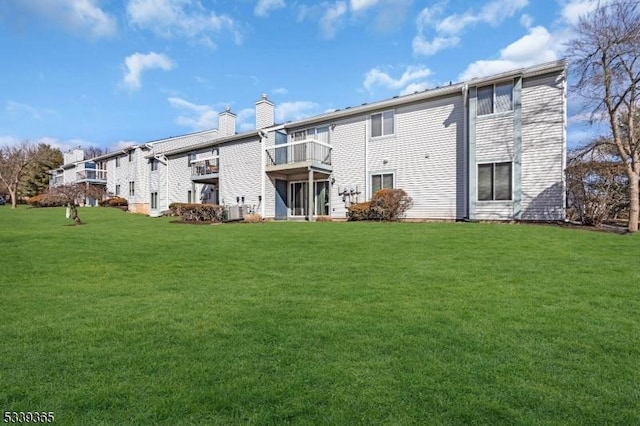 rear view of property featuring a lawn, a chimney, and a balcony