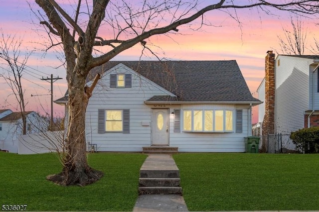 view of front of property featuring roof with shingles, a lawn, and fence