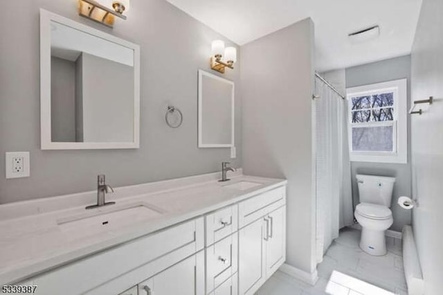 bathroom with toilet, marble finish floor, double vanity, and a sink