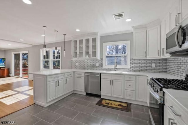 kitchen with white cabinets, glass insert cabinets, a peninsula, stainless steel appliances, and a sink