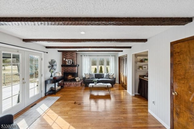 living area featuring a textured ceiling, french doors, a brick fireplace, and wood finished floors