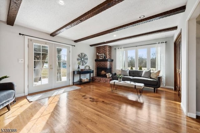 living room with french doors, a brick fireplace, a textured ceiling, wood finished floors, and baseboards