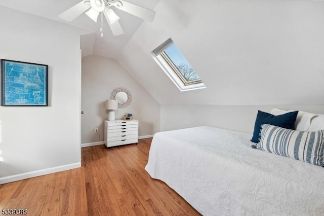 bedroom featuring light wood-style floors, vaulted ceiling with skylight, baseboards, and a ceiling fan