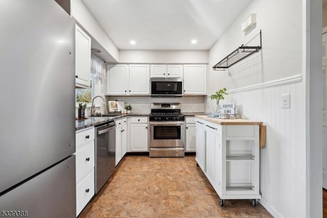 kitchen featuring dark countertops, backsplash, appliances with stainless steel finishes, white cabinets, and a sink