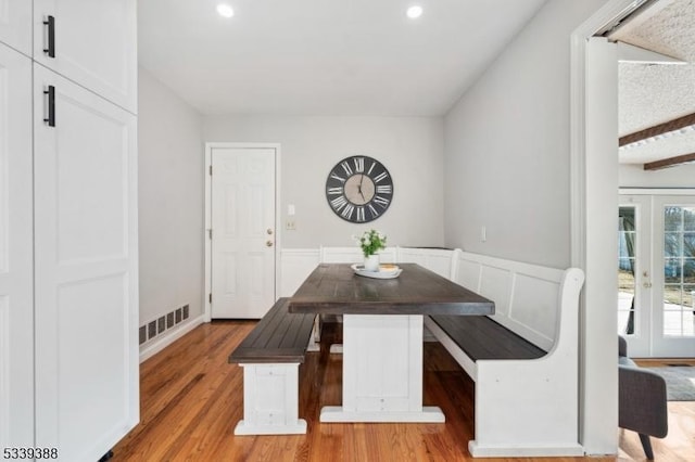 dining room featuring breakfast area, visible vents, wainscoting, wood finished floors, and beamed ceiling