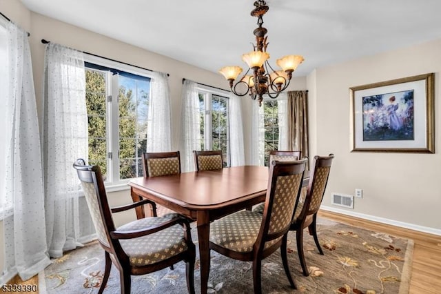 dining space featuring a chandelier, wood finished floors, visible vents, and baseboards