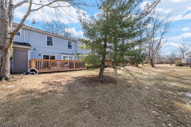 rear view of house with a deck, a chimney, and a lawn