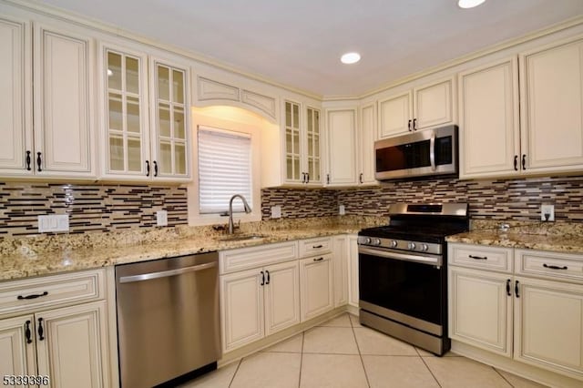 kitchen featuring light tile patterned floors, cream cabinets, appliances with stainless steel finishes, and a sink