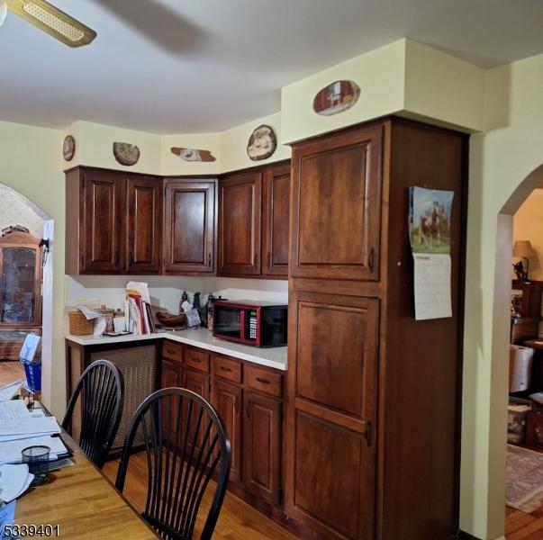 kitchen featuring light wood-type flooring, light countertops, arched walkways, and dark brown cabinets