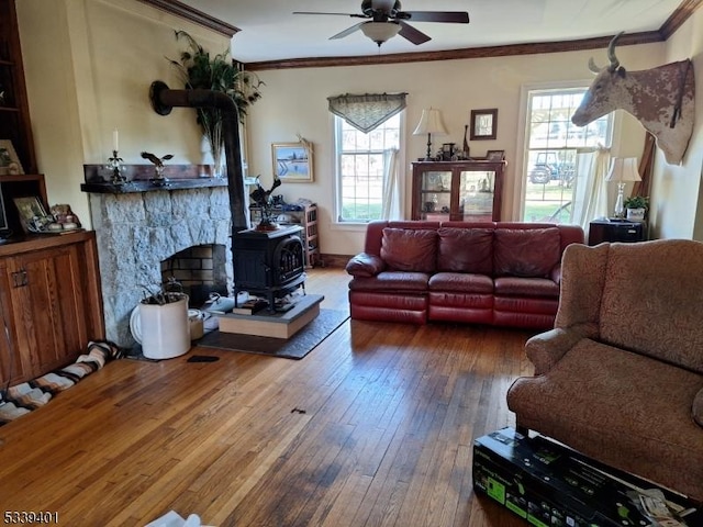 living room with ceiling fan, ornamental molding, wood-type flooring, and a wood stove