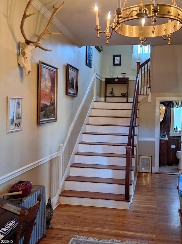 stairs featuring a notable chandelier, ornamental molding, and wood finished floors