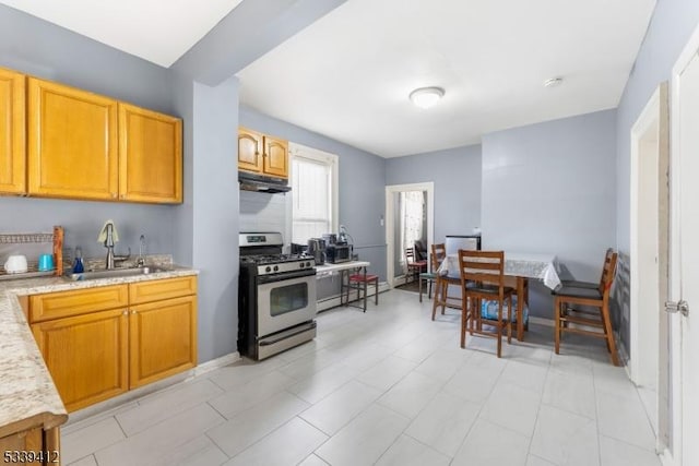 kitchen with light stone counters, a sink, under cabinet range hood, and gas range