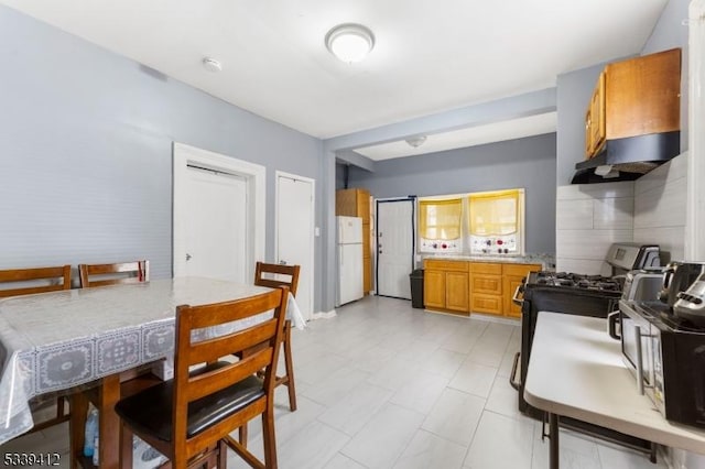 kitchen with light countertops, black gas range oven, brown cabinetry, freestanding refrigerator, and under cabinet range hood