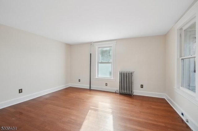 empty room featuring baseboards, radiator heating unit, and wood finished floors