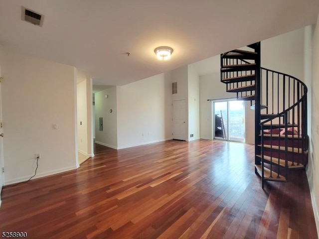 unfurnished living room with dark wood-style floors, visible vents, baseboards, and stairs