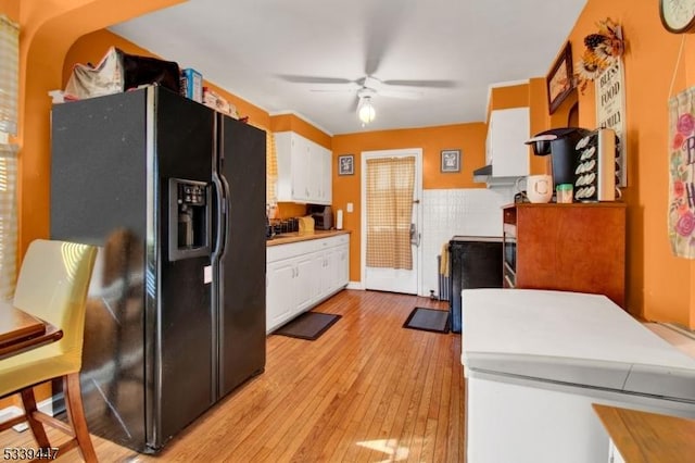 kitchen with light wood-type flooring, light countertops, white cabinetry, and black fridge