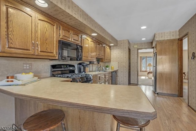 kitchen featuring a breakfast bar, gas stove, wallpapered walls, and black microwave