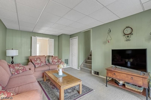 carpeted living area featuring a drop ceiling, visible vents, baseboards, and stairs