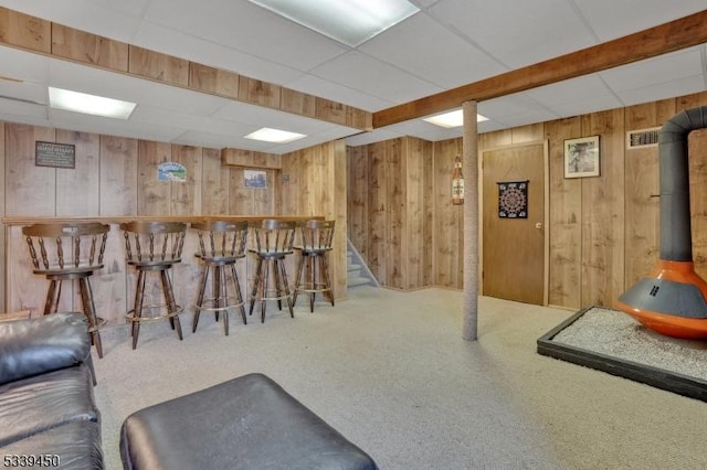 bar with a bar, carpet, a paneled ceiling, and wood walls