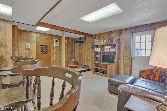 living room with carpet flooring, a paneled ceiling, wooden walls, and a wood stove